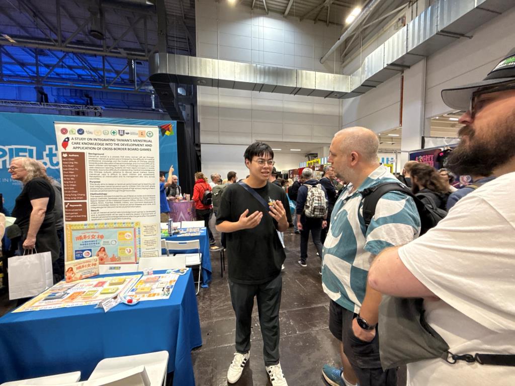 護理系學生傅冠鈞向詢問的國際友人熱情介紹「順利女神生理期照護」桌遊之設計
